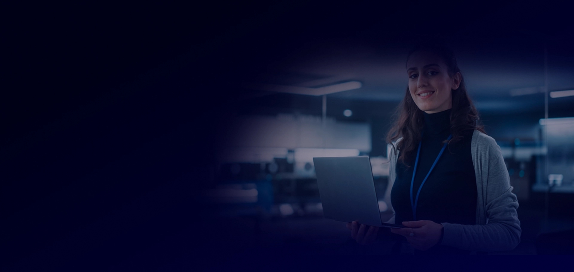 Duas pessoas em um ambiente de escritório olhando para um laptop, usando crachás de identificação. A sala tem uma atmosfera moderna e tecnológica com telas e paredes de vidro.