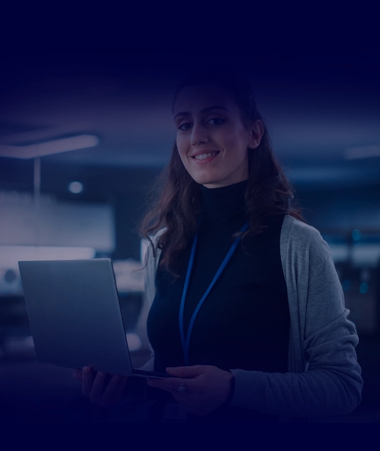 Duas pessoas em um ambiente de escritório olhando para um laptop, usando crachás de identificação. A sala tem uma atmosfera moderna e tecnológica com telas e paredes de vidro.